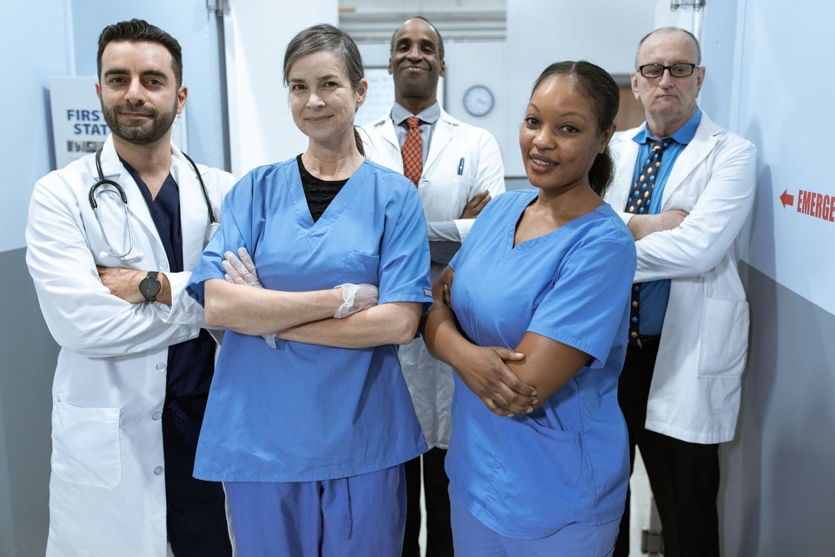 Diverse medical team in scrubs and white coats standing in a hospital corridor